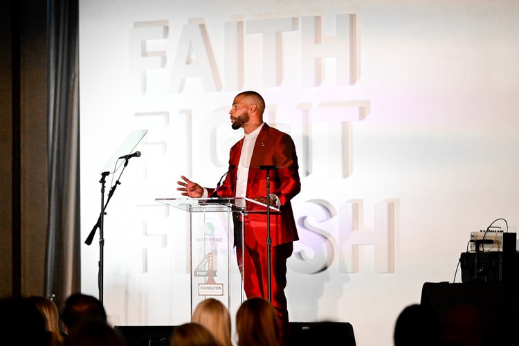 Person in red suit giving a speech at ‘Faith Fight Finish’ event.